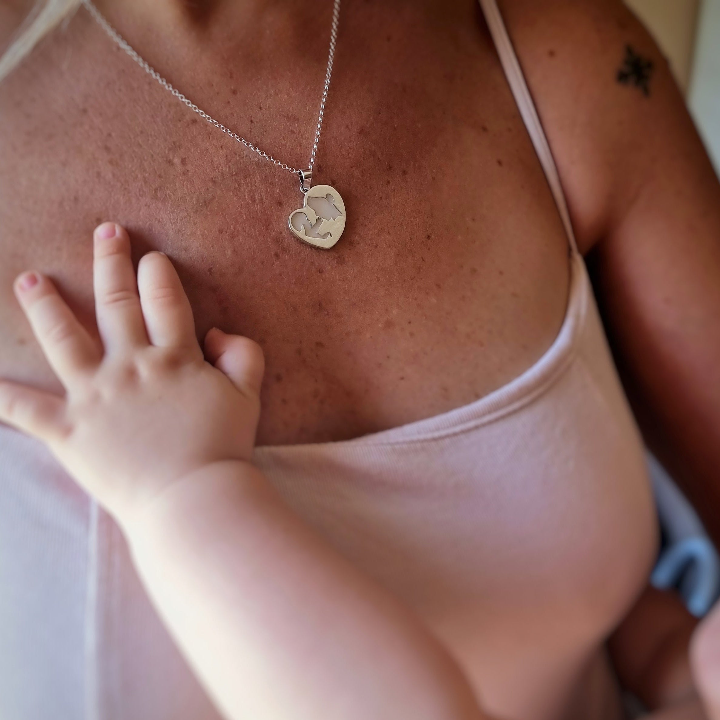 Colgante con forma de corazón con mamá y bebé de leche materna colocado en el cuello de la mamá, un recuerdo de lactancia